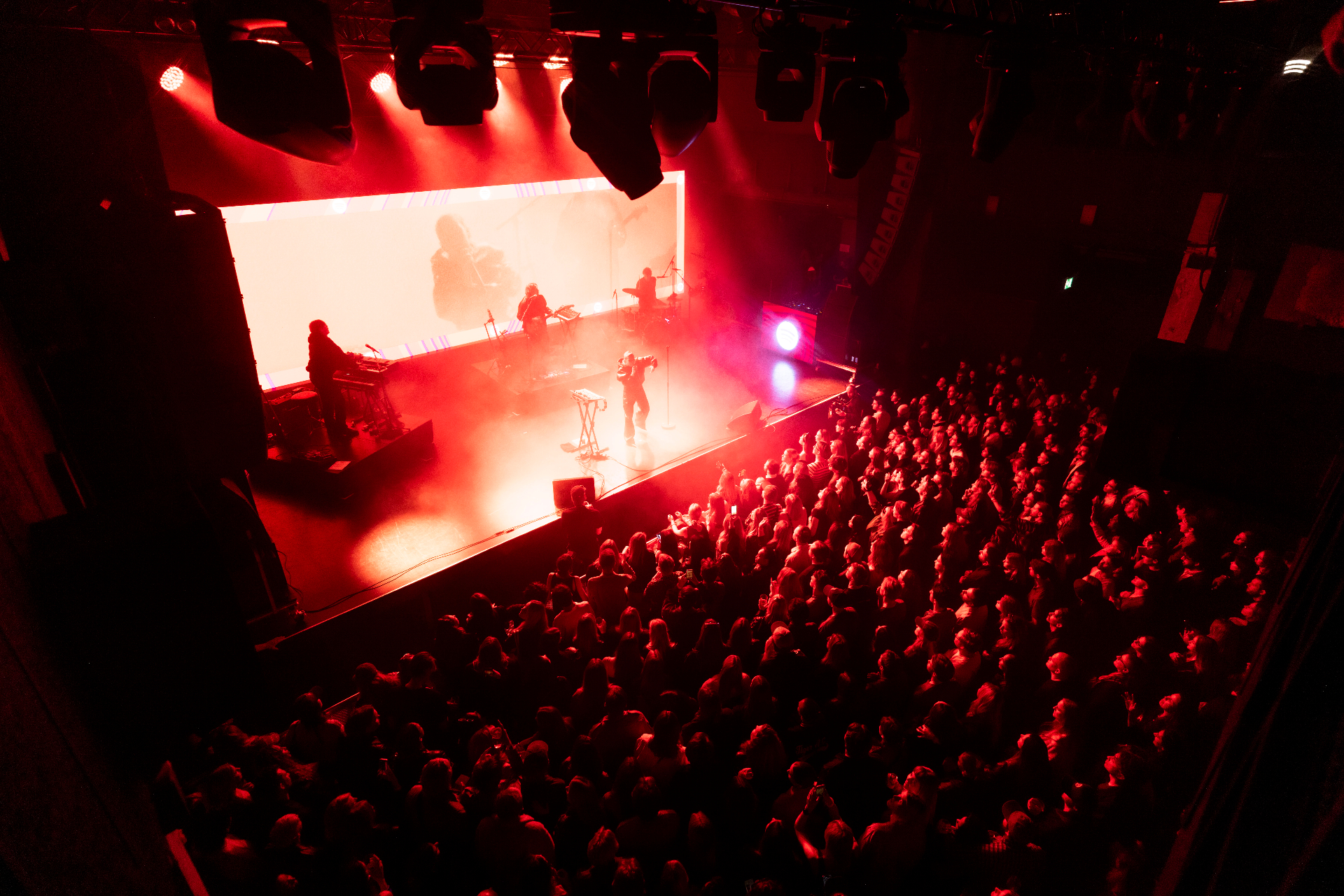 Wide view of Lykke Li and her band on the Fållan stage seen from the back of the room, the audience packed shoulder to shoulder under deep red light