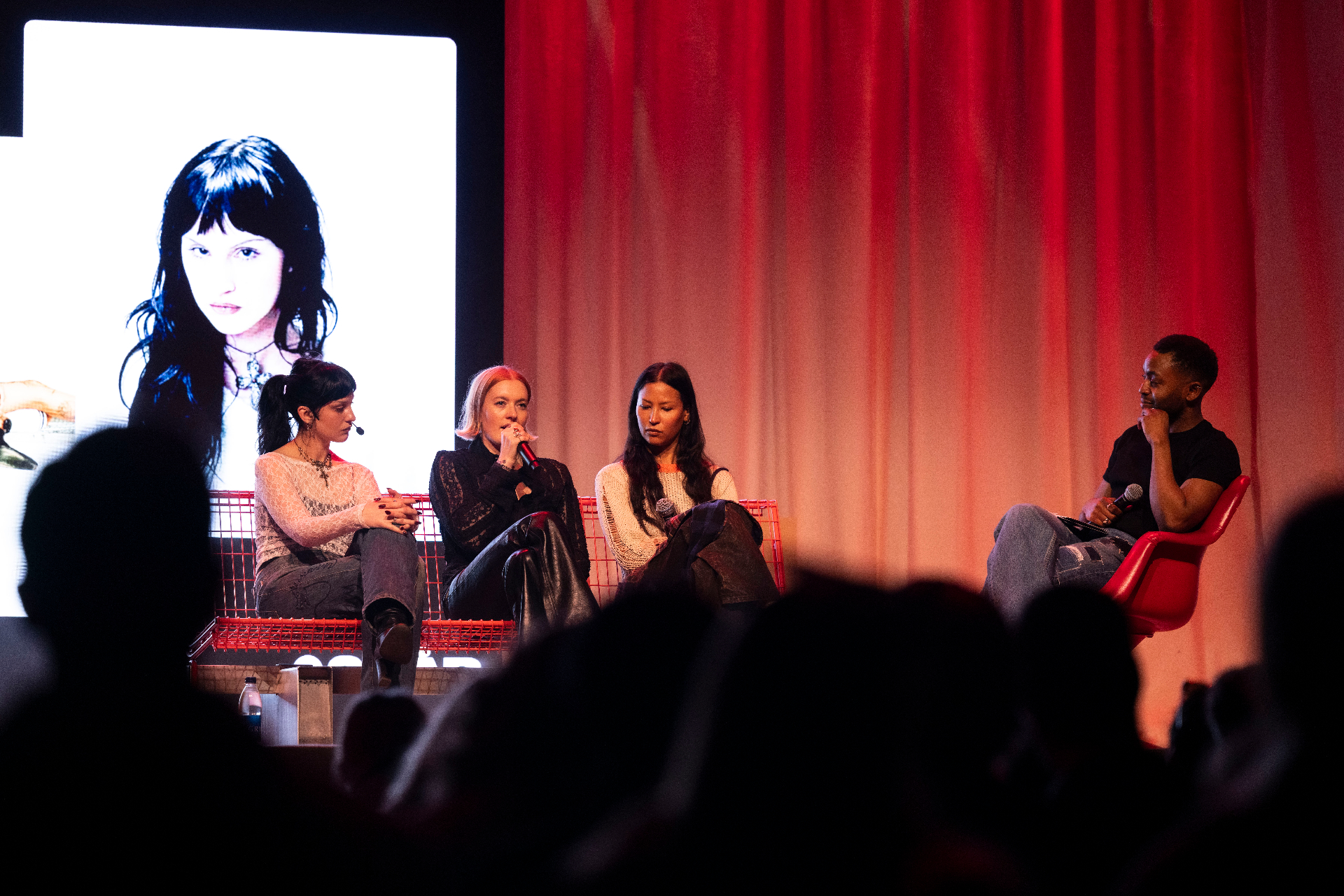 Olga Myko, Caroline Hjelt and Aino Jawo of Icona Pop on the red wire bench at Fållan with moderator Paulo Saka of Spotify, a large portrait of Olga Myko projected behind them.