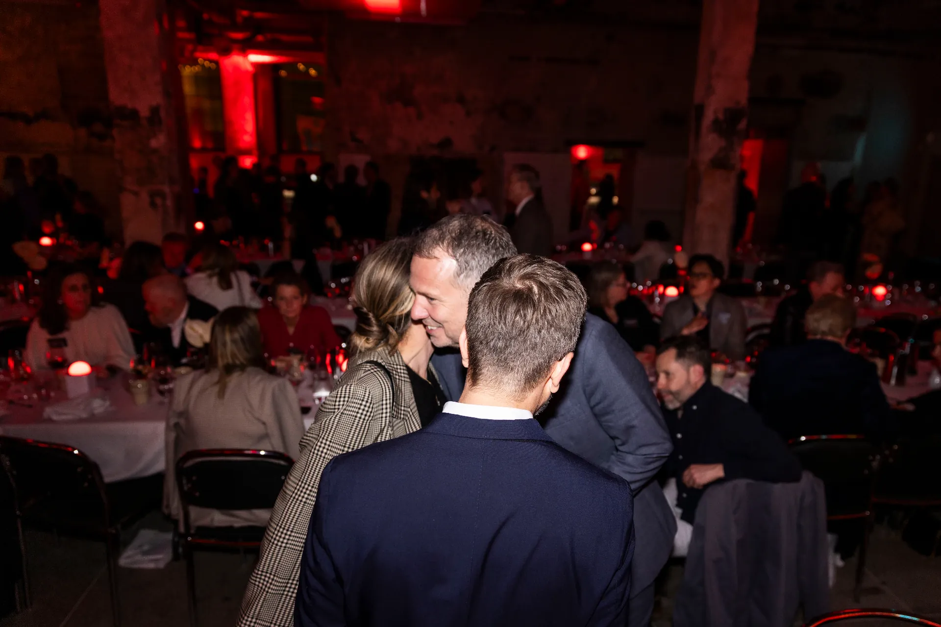Guests greeting each other between candlelit dinner tables